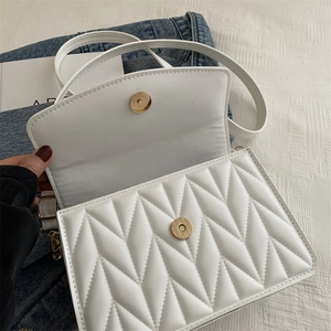 Detailed view of white crossbody bag with V-shaped quilting and gold magnetic clasp