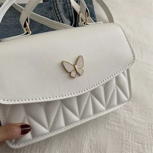 Detail of white PU leather bag featuring gold-trimmed butterfly buckle and quilted texture
