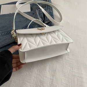 Detail of white quilted crossbody bag featuring a golden butterfly clasp and premium texture