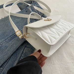 Detailed shot of white quilted crossbody bag with gold butterfly metal clasp and strap