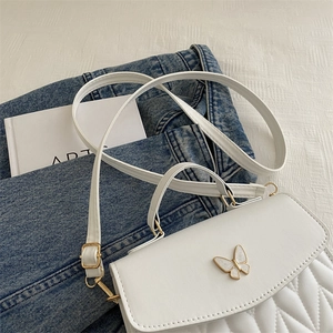 Detailed view of white quilted crossbody bag with a golden butterfly clasp and strap
