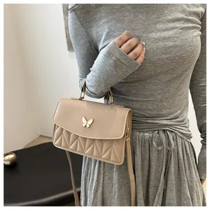 Detail of beige quilted flap crossbody bag with gold butterfly clasp and chain strap
