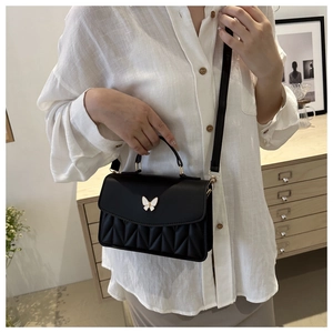 Detail of black quilted shoulder bag featuring an elegant white butterfly metal buckle closure
