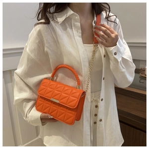 Detail of orange quilted crossbody bag with woven handle and gold chain strap on model