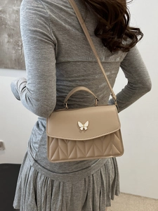 Beige quilted crossbody bag with butterfly buckle shown on a model in a minimal setting