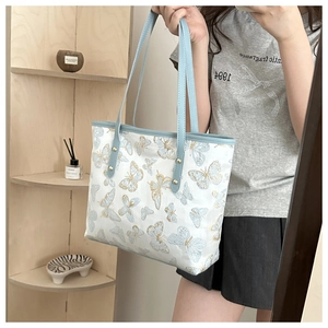 Close-up of elegant butterfly embroidery and gold rivets on a light blue tote bag