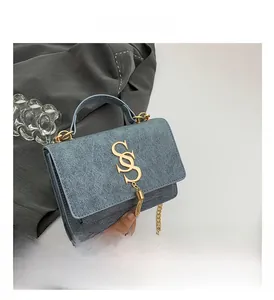 Detail of blue denim crossbody bag featuring gold S-shaped logo and chain strap