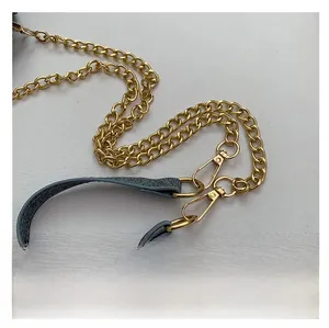 Close-up of golden metal chain strap with grey leather shoulder pad and lobster clasps