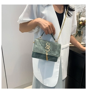 Detail of dark green velvet shoulder bag with golden S logo, fringe and chain strap