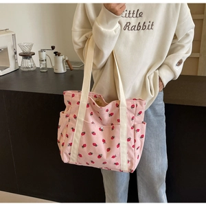 Detail of pink corduroy tote bag featuring red strawberry patterns and white straps