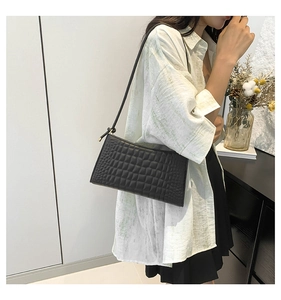 Close-up of a stylish black crocodile texture underarm bag worn by a model in a casual setting