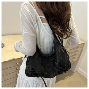 Detail of black bow shoulder bag with textured pleats on a back-view model outfit
