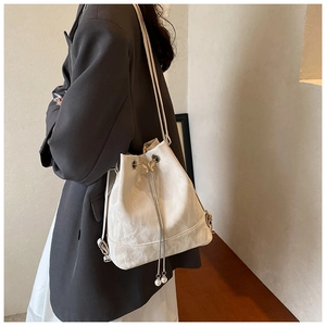 Close-up of white bucket bag featuring a metal butterfly clasp and pearl drawstring details