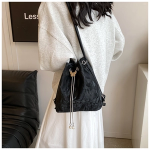 Detail view of black drawstring bucket bag with butterfly metal buckle and pearl tassels