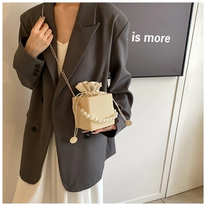 Detail of beige woven bucket bag with pearl handle and golden chain crossbody strap