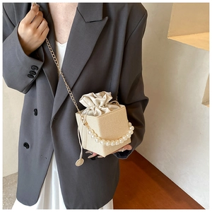 Elegant woven bucket bag shown on a model with pearl handle and golden chain strap