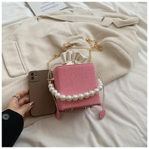 Pink textured cube bag detail with white pearl handle and golden chain strap on fabric