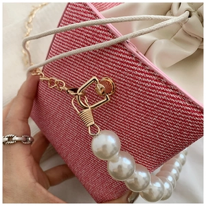 Detail of pink denim bucket bag featuring pearl handle and gold chain strap close-up