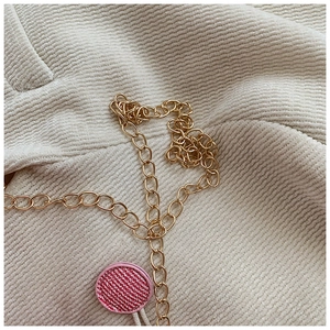 Close-up of golden metal chain and pink woven round charm on stylish crossbody bag
