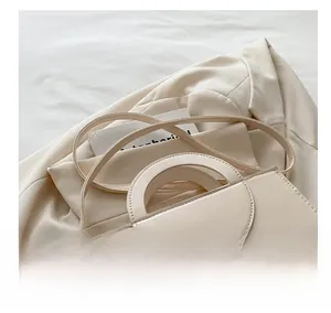 Detail of cream PU leather handbag with unique handle on beige blazer background