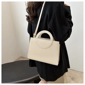 Close-up of minimalist cream white square handbag featuring elegant round top handles