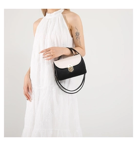 Detail of a chic two-tone crossbody bag with gold twist lock on a white dress model