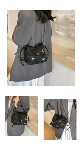 Detalle de bolso saco plisado negro con adorno de mariposa plateada y cadena
