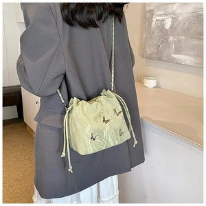 Detalle de bolso saco verde menta con cordón y dijes de mariposa plateados en la cadena