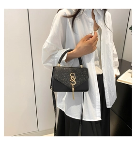 Detail of black woven handbag with sequined flap and golden tassel logo charm