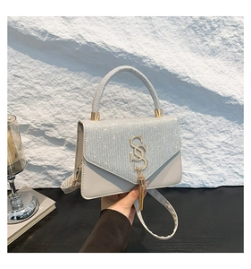 Detail of the woven handbag featuring sparkling rhinestones, S-logo, and golden tassels