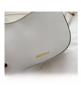 Detail view of white leather shell bag with gold logo lettering and smooth texture