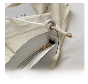 Close-up of golden metal zipper and knotted leather strap on white shoulder bag