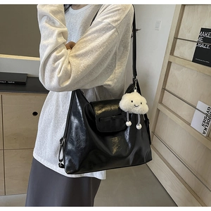 Detail of black glossy tote bag featuring a bow flap and white plush cloud charm accessory
