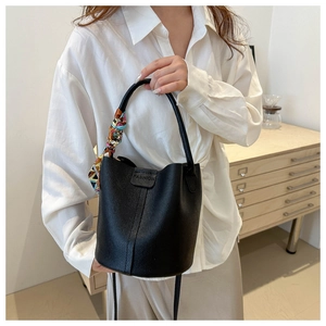Detail van zwarte bucket bag van generfd leer met reliëfopdruk en een zijden sjaalhandvat