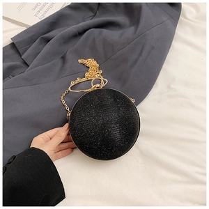 Close-up of a black spherical evening clutch bag featuring glitter finish and gold ring handle