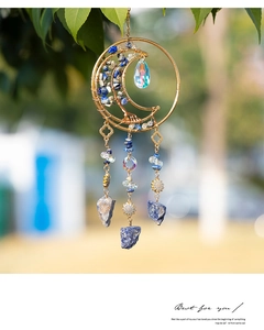 Close-up of moon-shaped crystal suncatcher with blue stones hanging on green tree branch