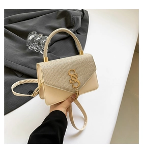 Détail du rabat tissé champagne avec logo doré et pompon sur le sac à main de luxe