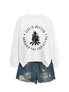 Flat lay of a white crewneck sweatshirt with campfire graphic and frayed denim shorts