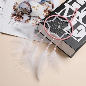 Dettaglio di un acchiappasogni rosa e bianco con piume e perline per decoro auto