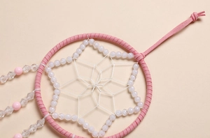 Dettaglio di acchiappasogni rosa e bianco con trama a stella e perle di cristallo traslucide