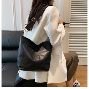 Detail of patchwork black leather tote bag with wide fabric strap and gold hardware
