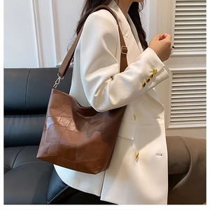 Detailed view of the brown leather shoulder bag with geometric stitching and gold buckles