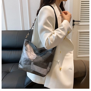 Detail of grey and black patchwork tote bag with leather straps on a white blazer