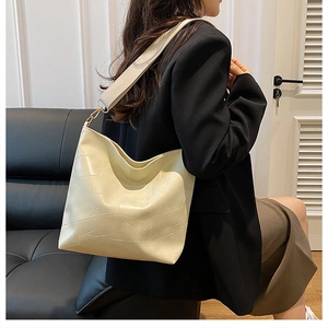 Minimalist beige shoulder bag with geometric stitching shown on model in modern room
