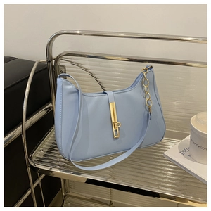 Detail of light blue crescent bag with golden clasp and chain on a silver shelf