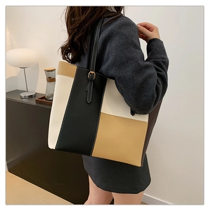 Detail of color-block tote bag with white contrast stitching and gold buckle on shoulder strap