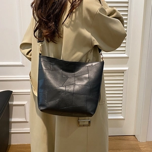 Minimalist black patchwork bucket bag with wide shoulder strap in a city commute style