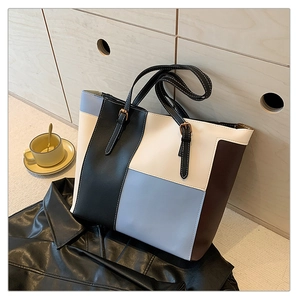 Close-up of color-block leather tote bag featuring adjustable gold buckle straps