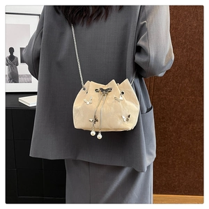 Detail of beige bucket bag featuring 3D silver butterflies and pearl drawstring accents