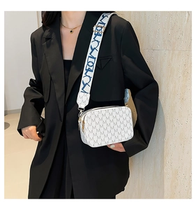 Detail of white crossbody bag with grey M pattern and wide artistic fabric strap